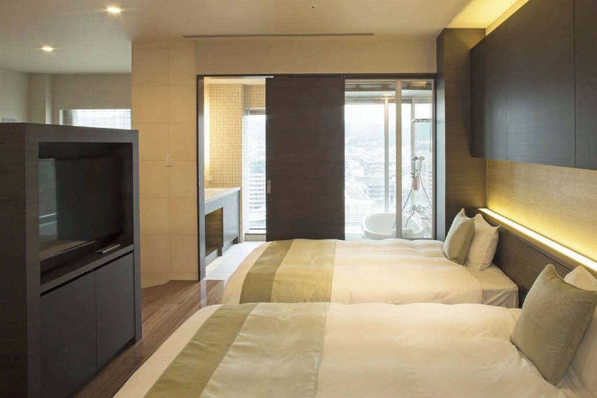 A hotel room with two beds, a TV, and a balcony with a city view.