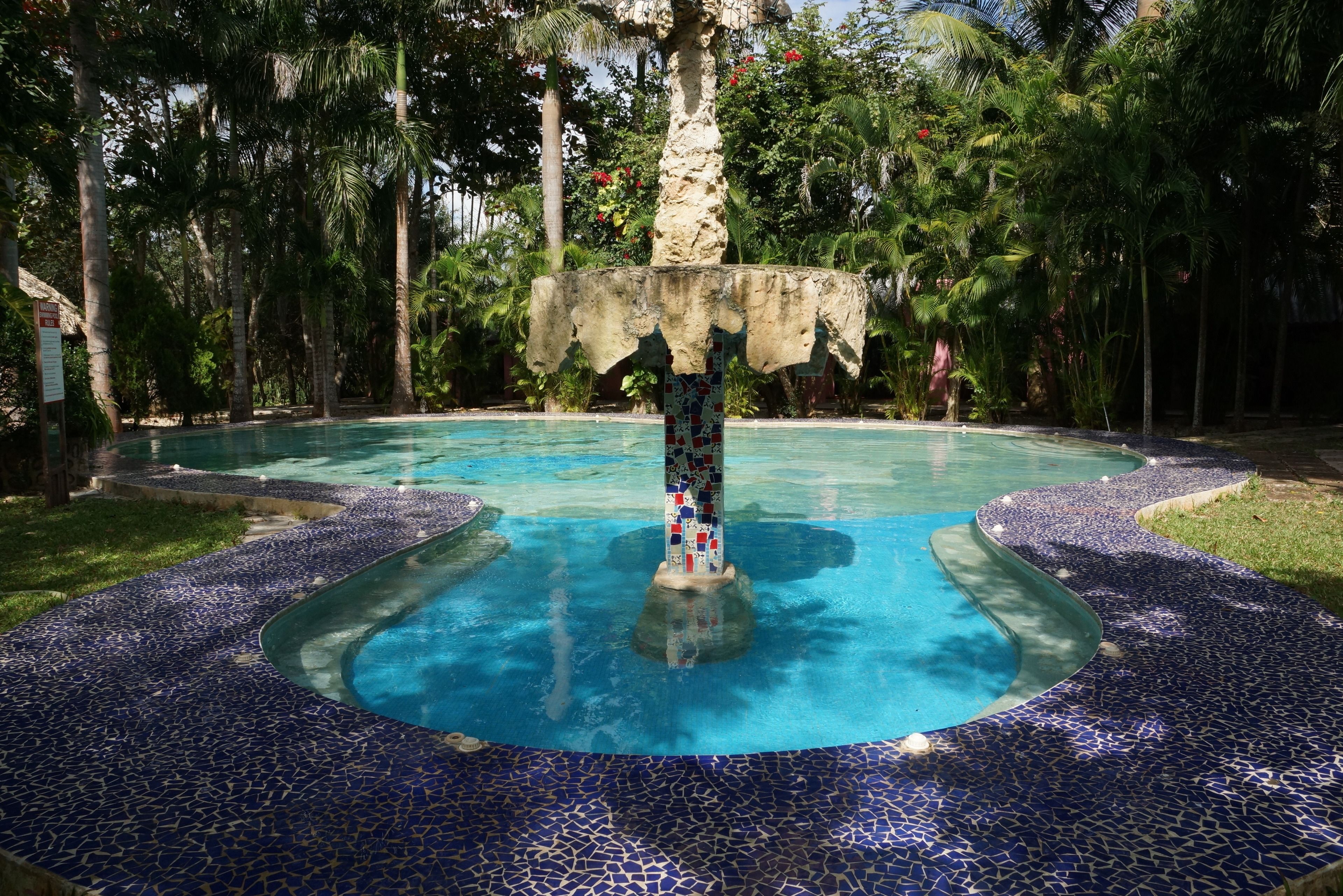 A swimming pool with a mosaic-tiled edge and a central fountain.