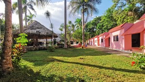 Un resort tropical con un pabellón de techo de paja, palmeras y una hilera de edificios rosados.