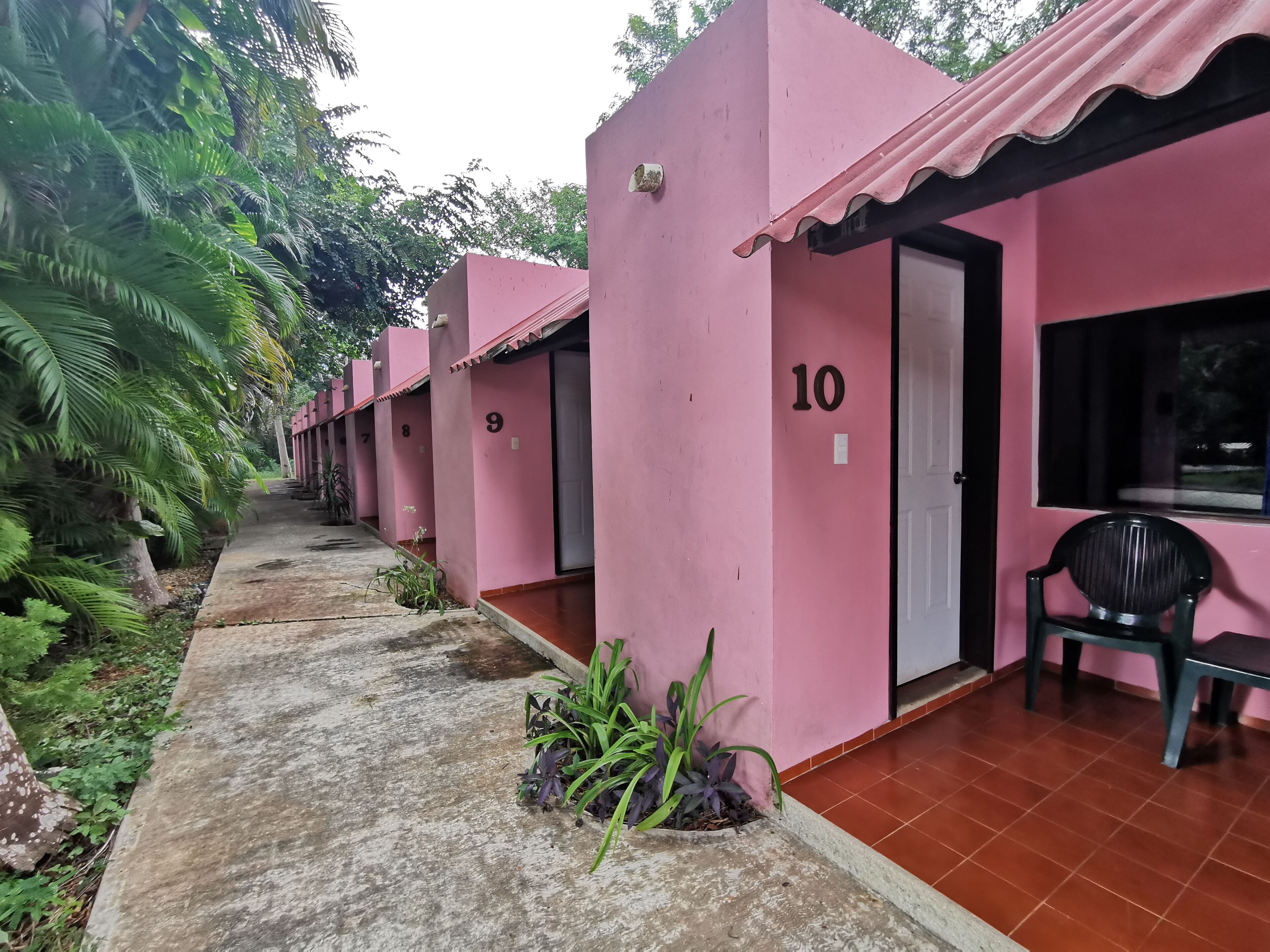 A row of pink buildings numbered 9 to 10, with a concrete pathway and greenery on the left.