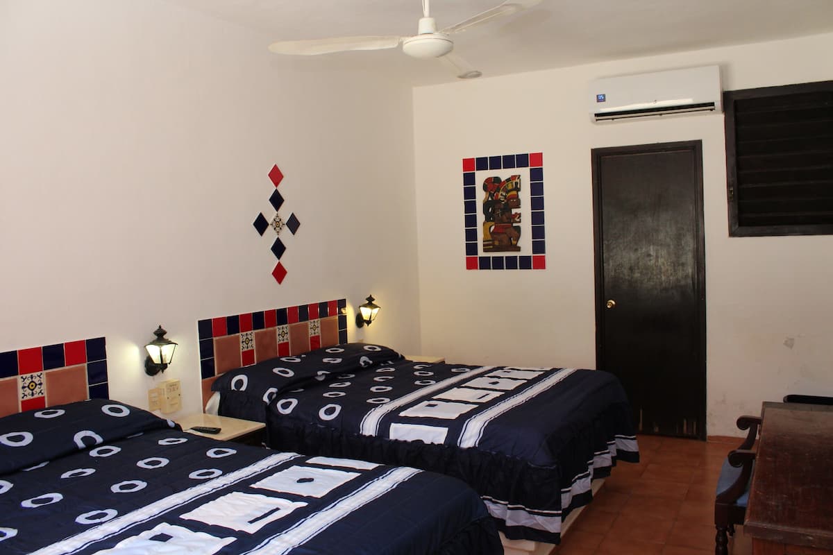 Habitación de hotel con dos camas, ventilador de techo, equipo de aire acondicionado, una obra de arte colgada en la pared y una puerta con ventanal.