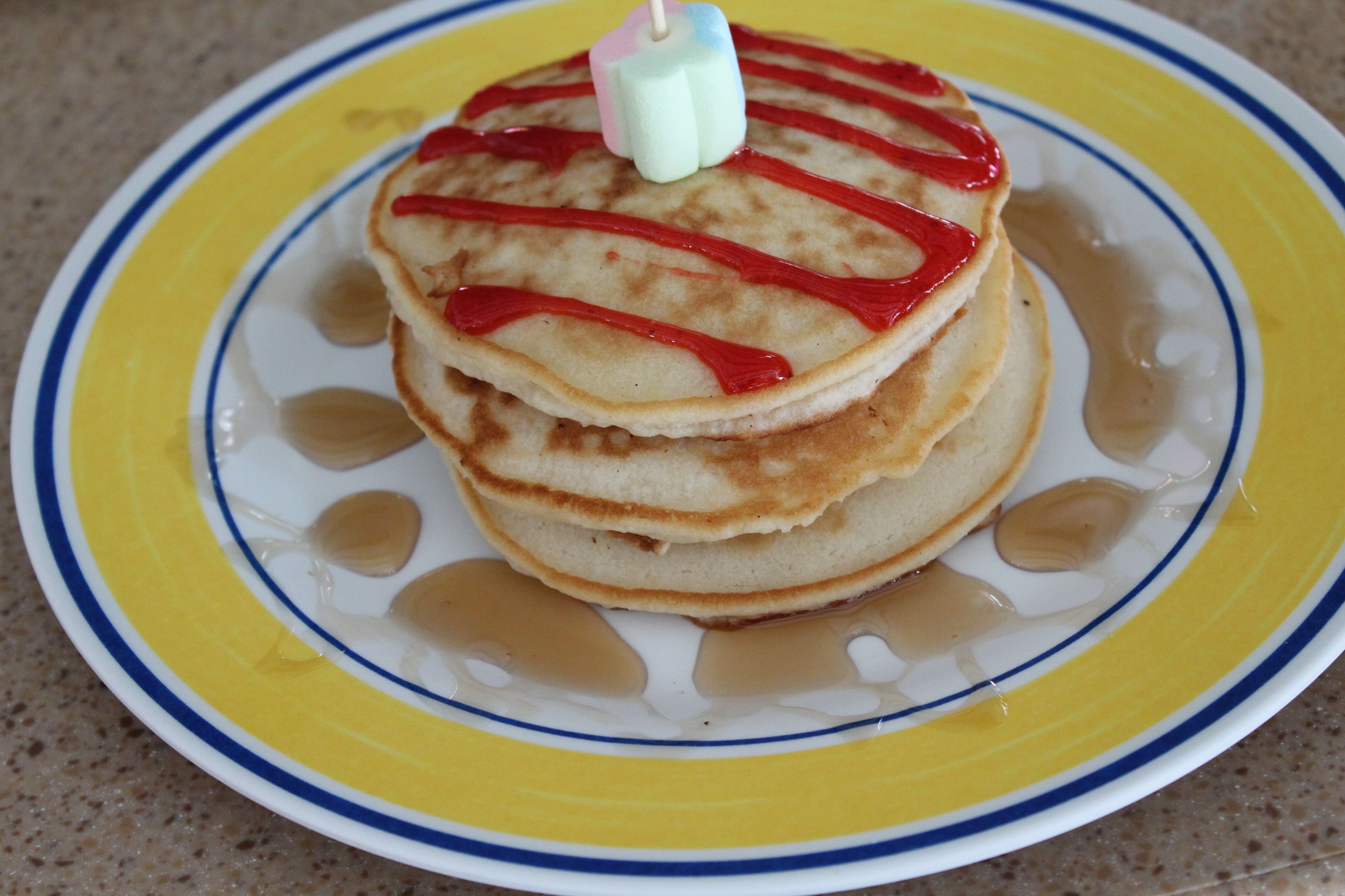 Una pila de tortitas con jarabe y una vela sobre un plato.