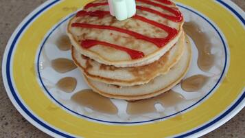 Una pila de tortitas con jarabe y una vela sobre un plato.