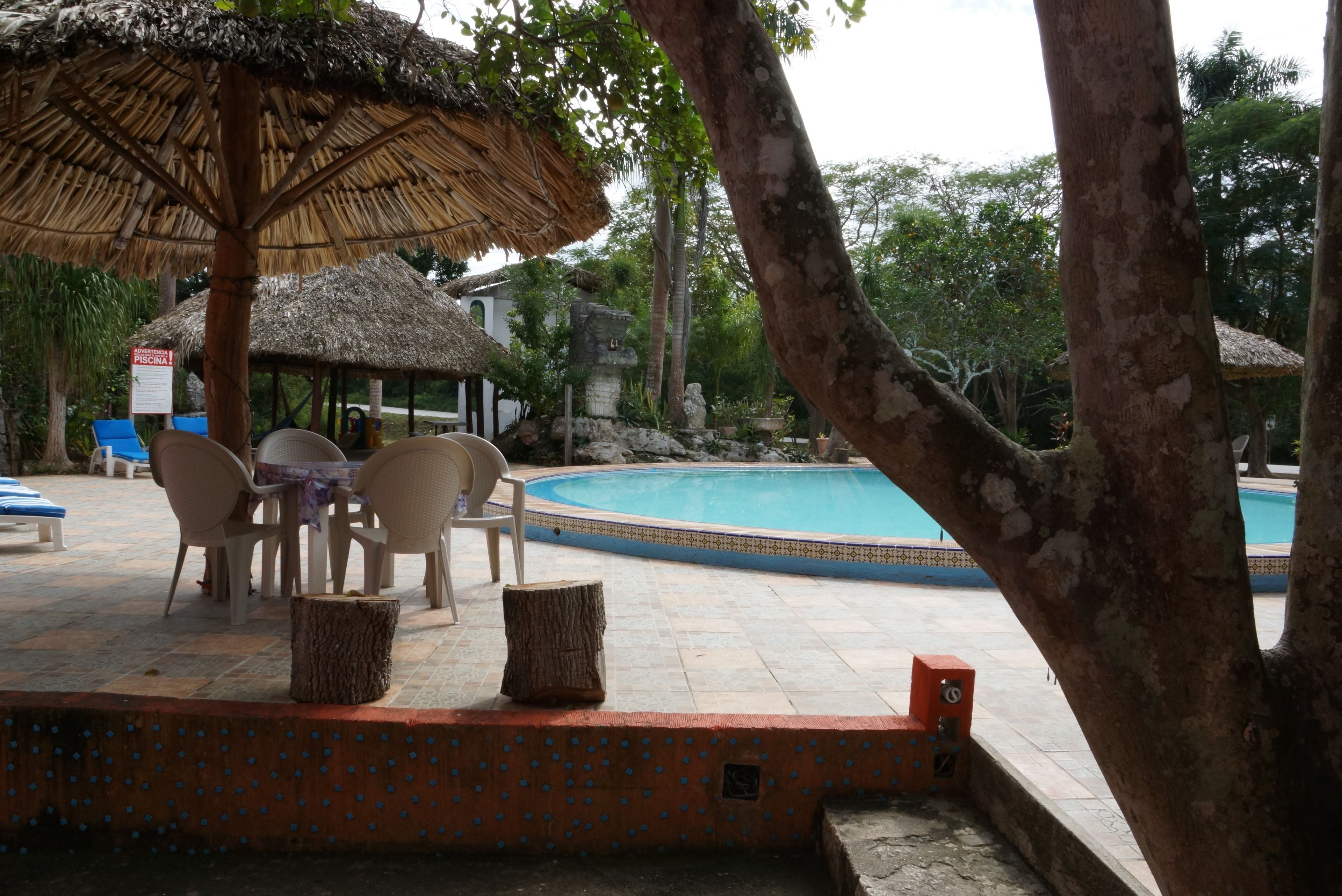 A pool area with a thatched umbrella, lounge chairs, and a sign indicating a pool.
