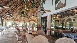 Un restaurante con manteles a cuadros, sillas de mimbre, ventiladores de techo y techo de paja.