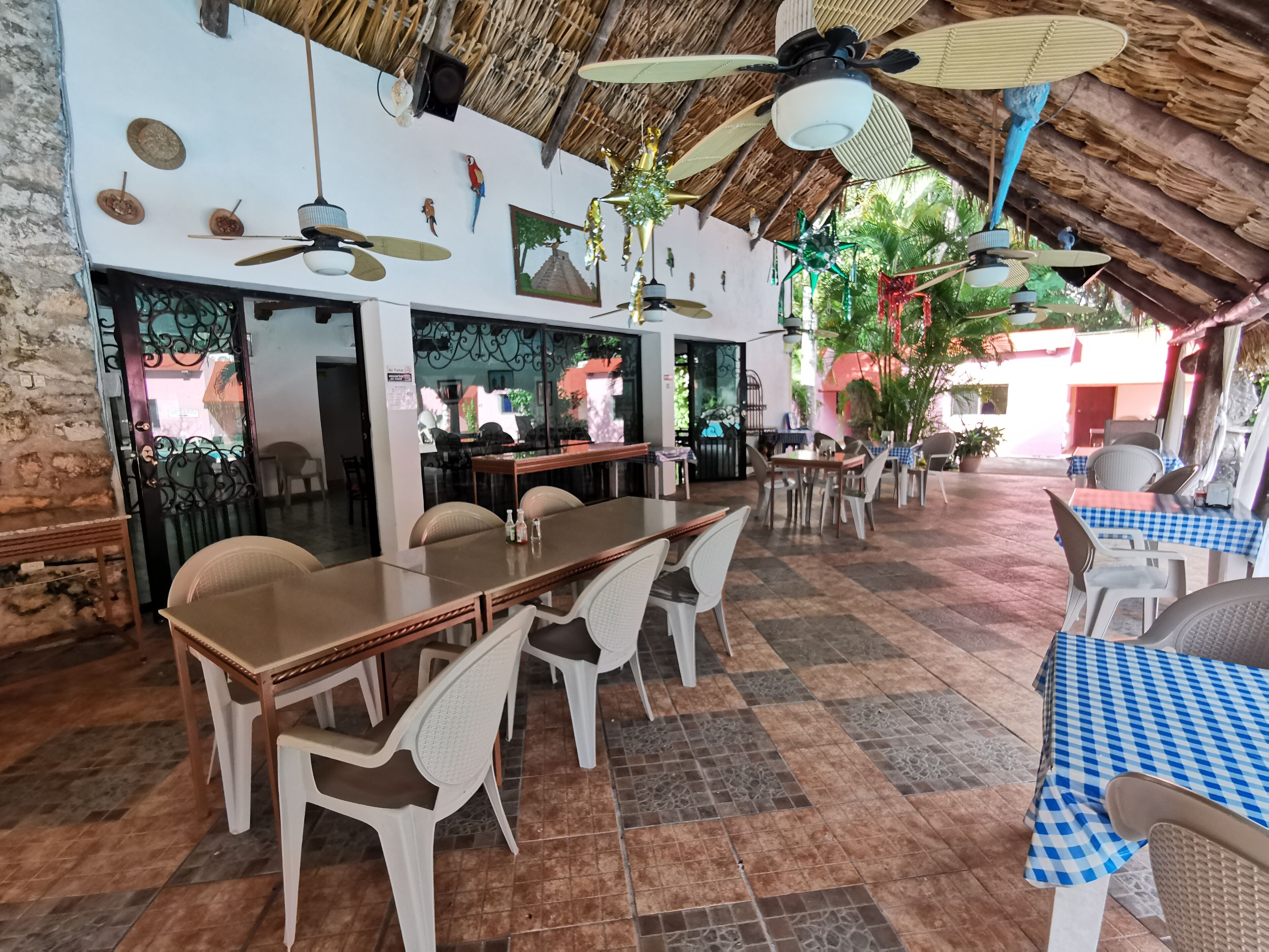 Un restaurante con techo de paja, piso de baldosas y diferentes opciones de asientos, incluyendo mesas y sillas.