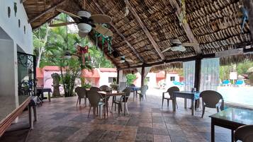 An outdoor dining area with thatched roof, tiled flooring, and tables with chairs.