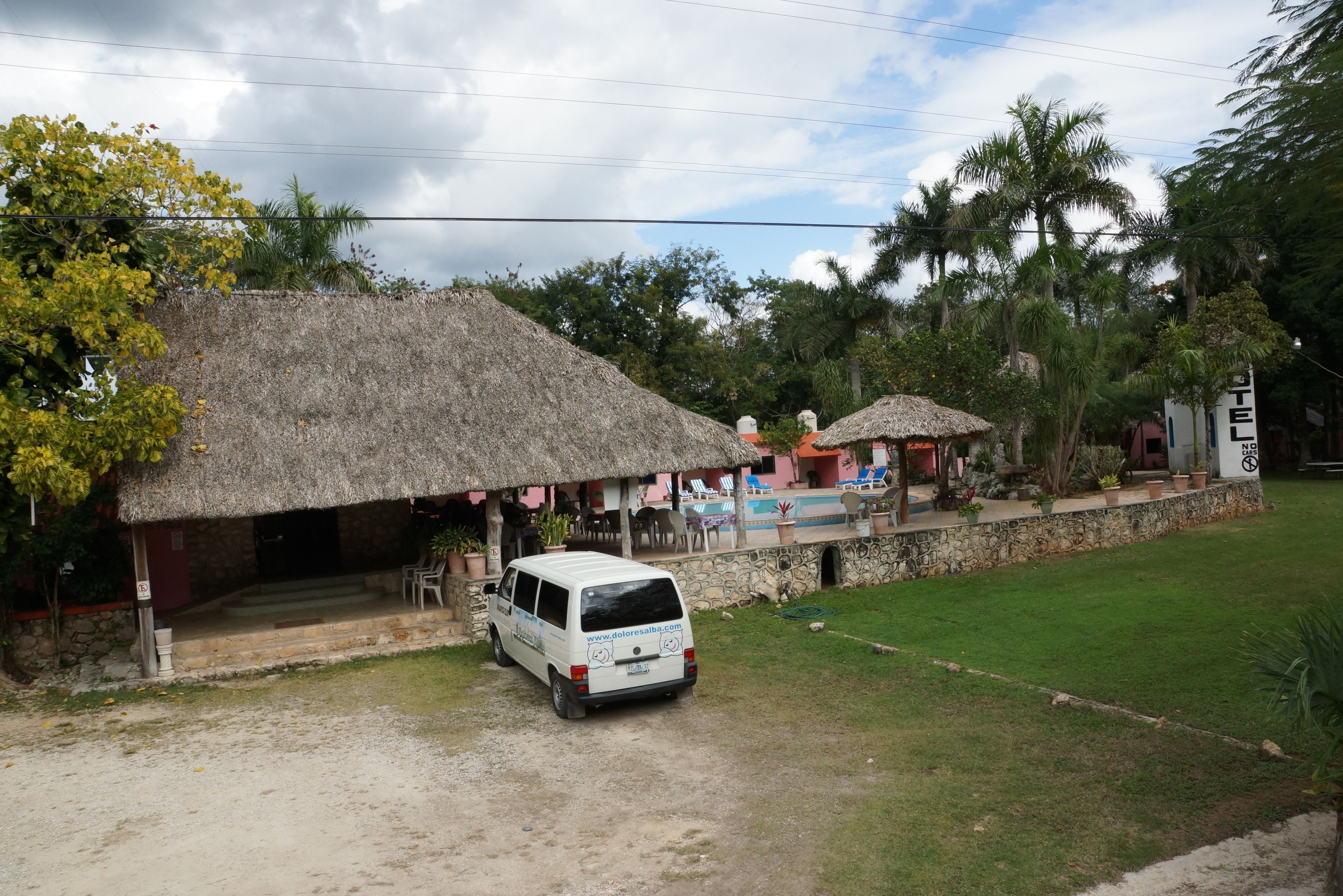 A white van parked in front of a building with a thatched roof and a stone wall.