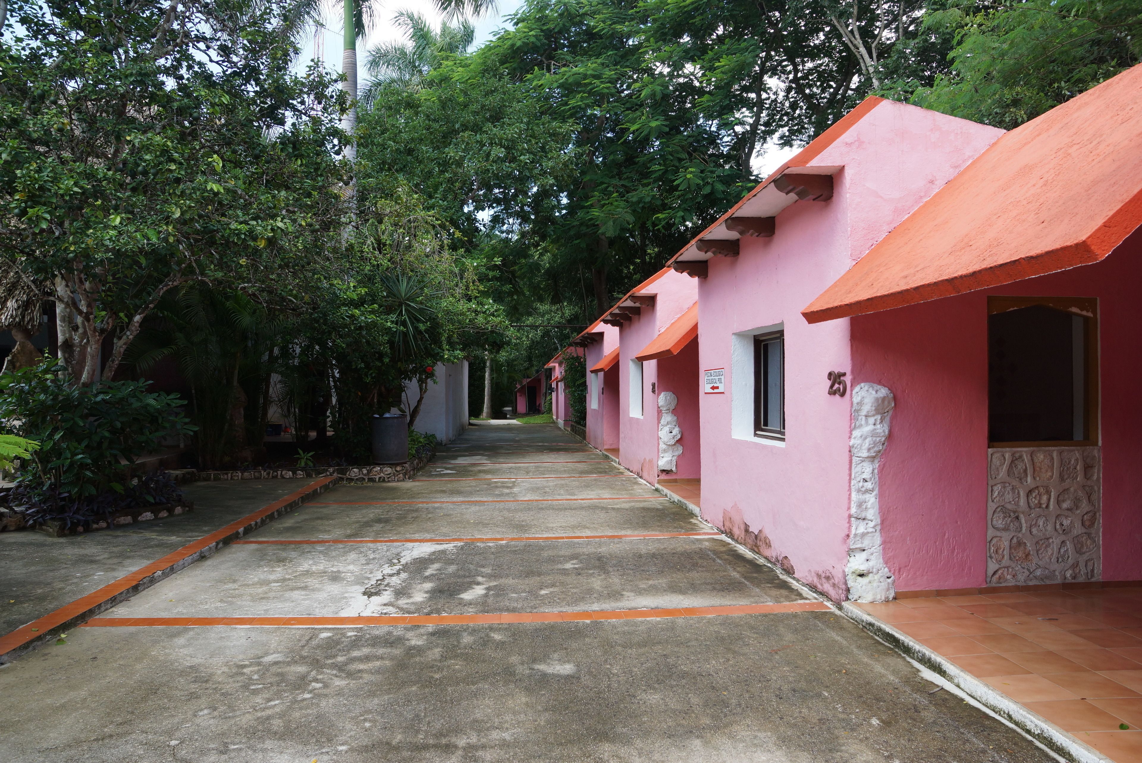 A row of pink buildings with a concrete pathway between them, surrounded by greenery.