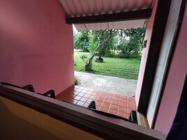 Vista desde una ventana con pared rosa, suelo de baldosas y un área verde con árboles y una planta pequeña.