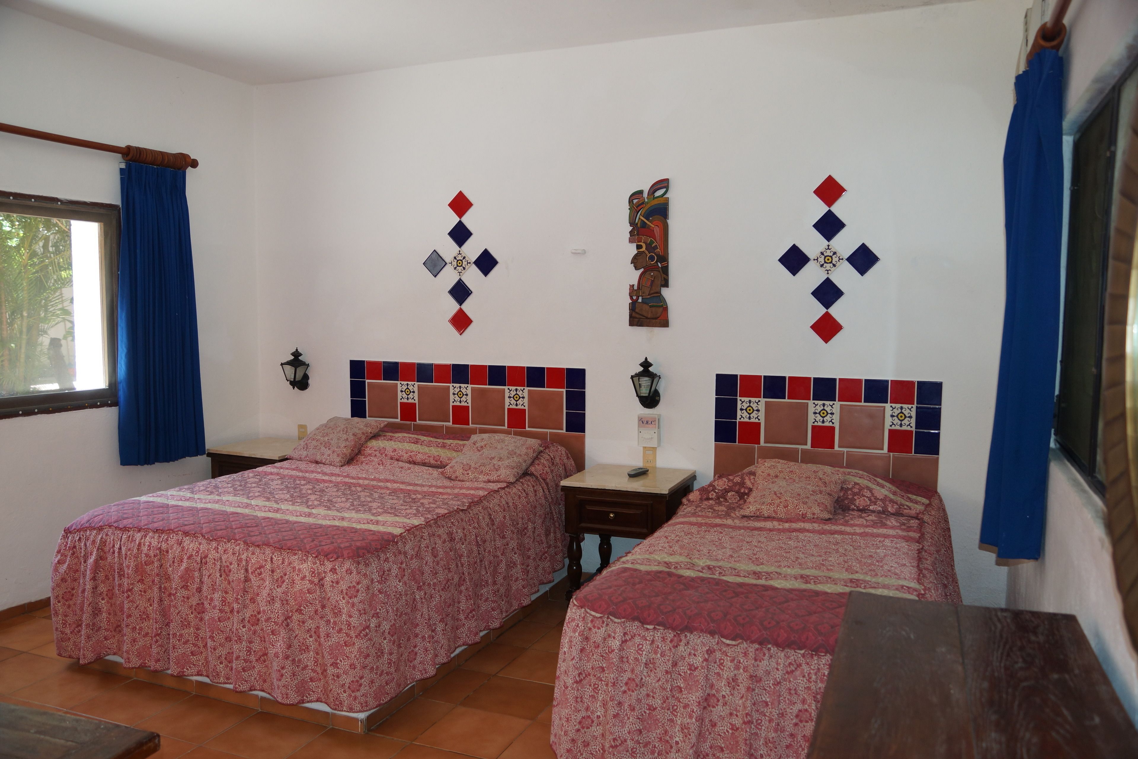 A bedroom with two beds, a window with blue curtains, and decorative wall tiles.