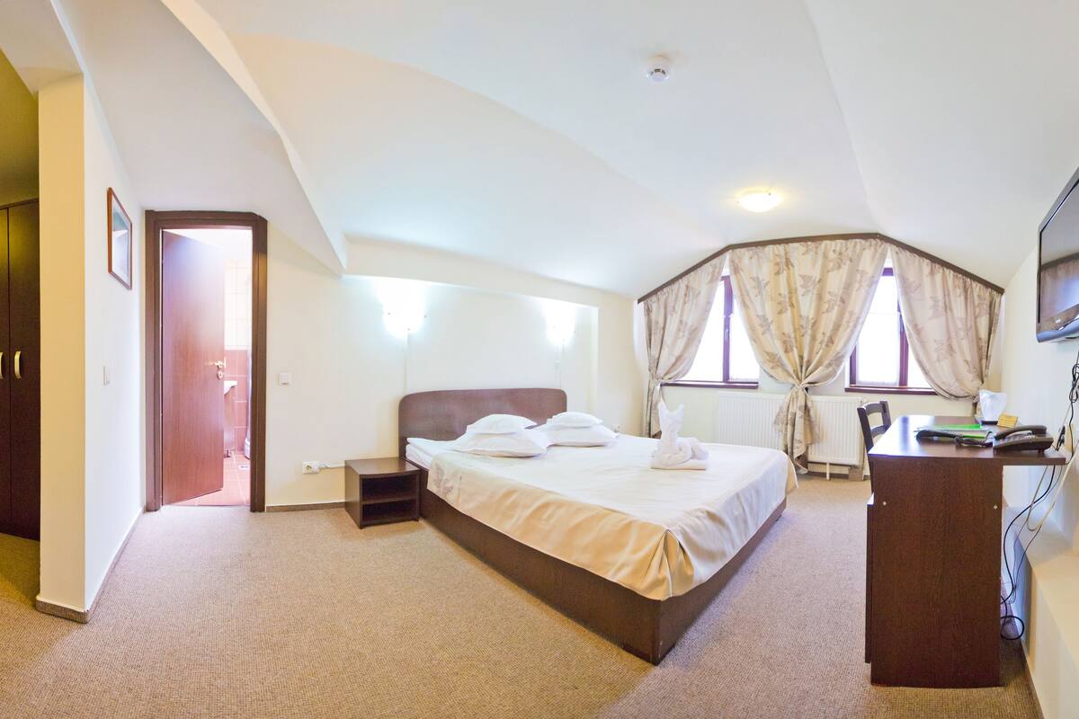 Ein Hotelzimmer mit Bett, Schreibtisch, Fernseher und einem Fenster mit Vorhängen.