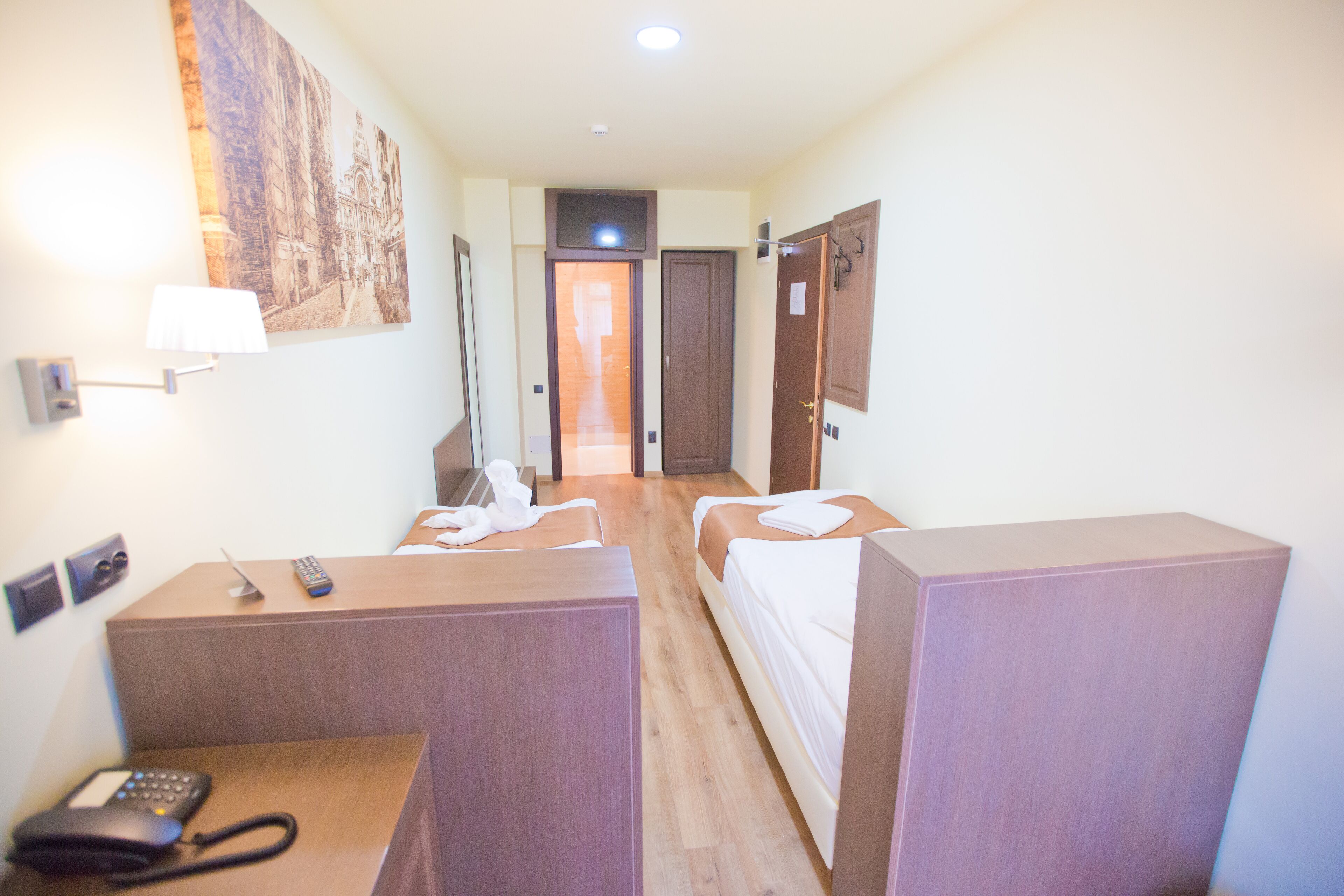 Una habitación de hotel con dos camas individuales, un escritorio con teléfono y un televisor montado en la pared.