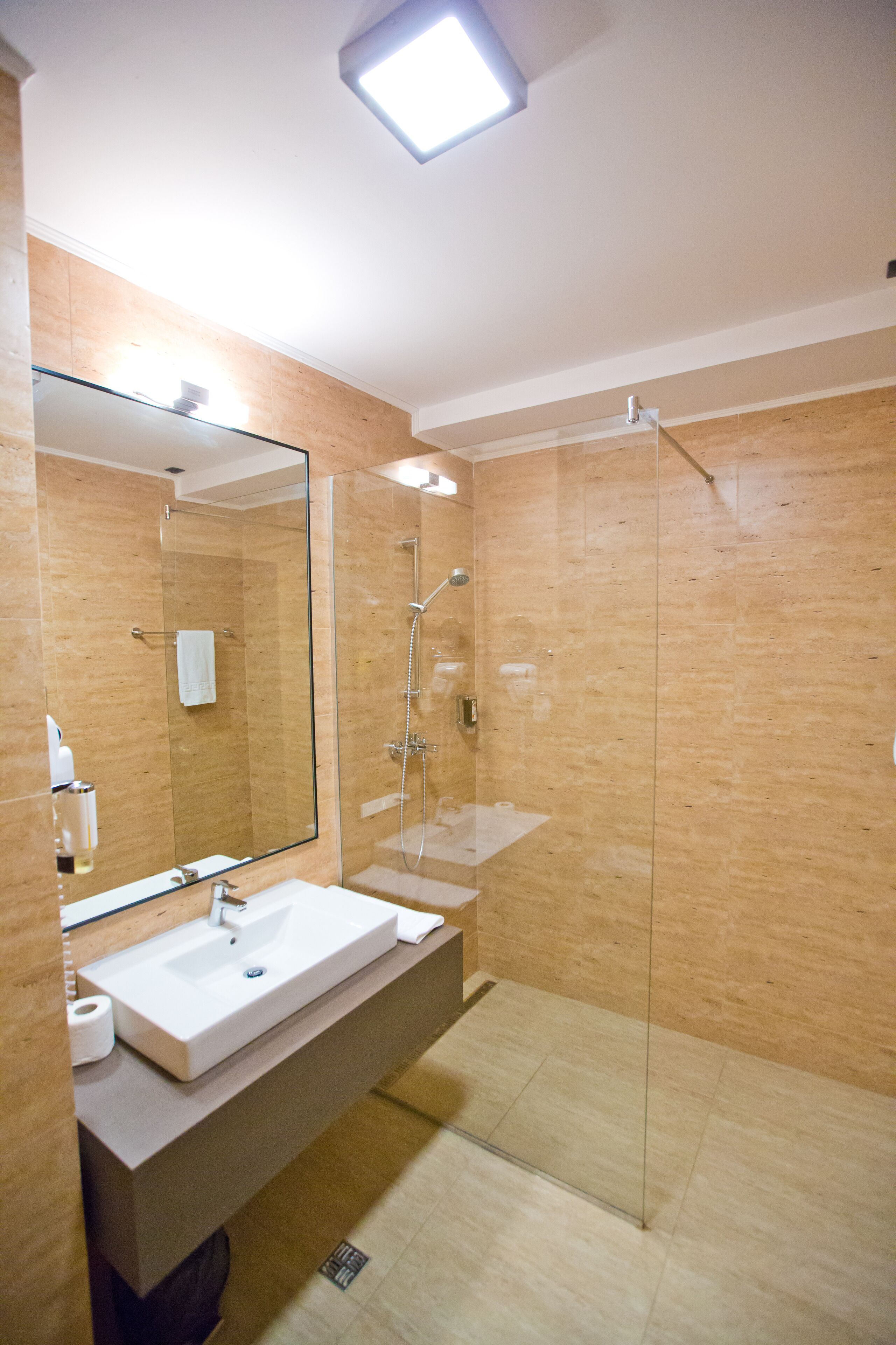Un baño moderno con cabina de ducha de vidrio, un espejo grande y un lavabo blanco.