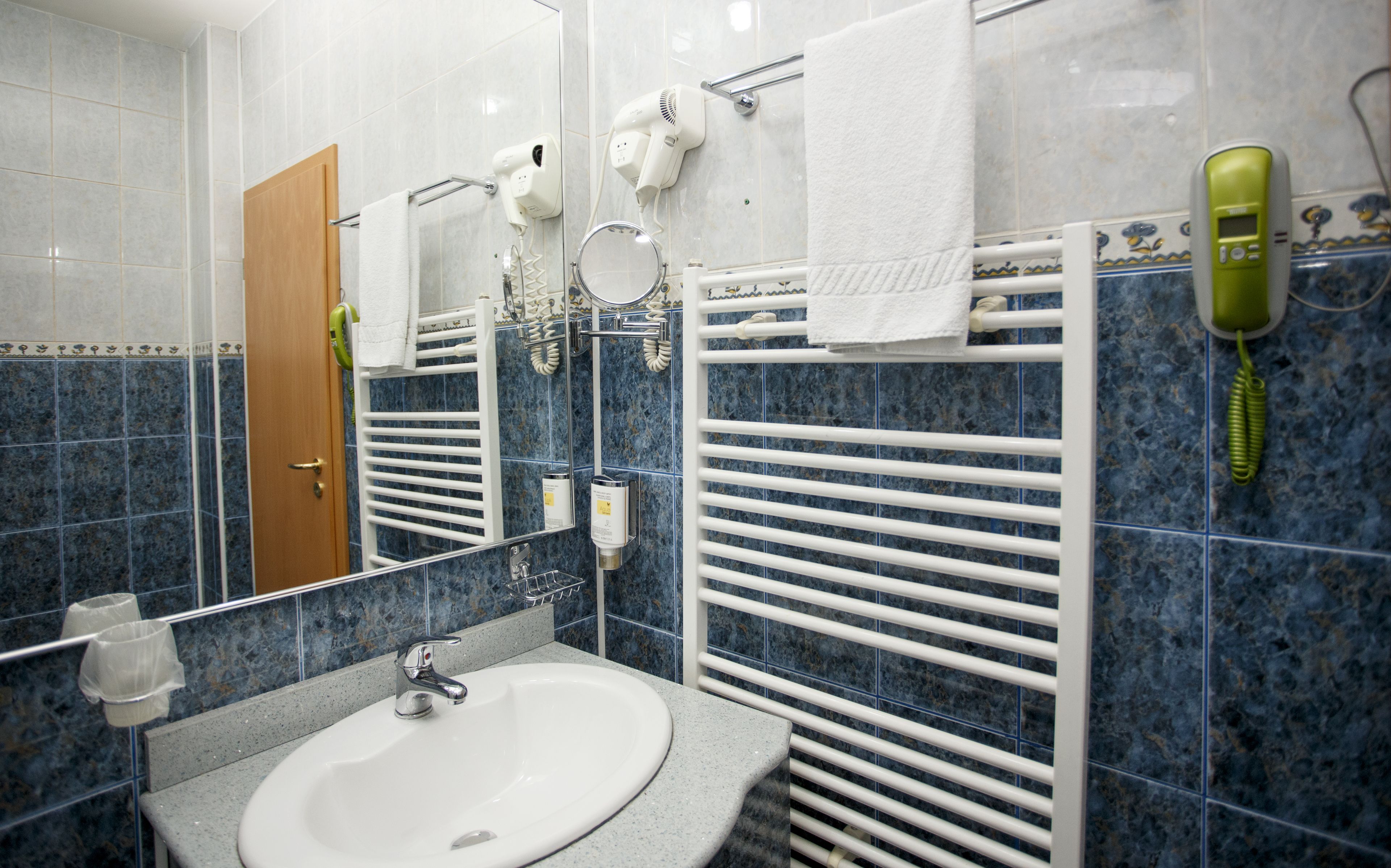 A bathroom with a sink, mirror, towel rack, hairdryer, and a telephone.