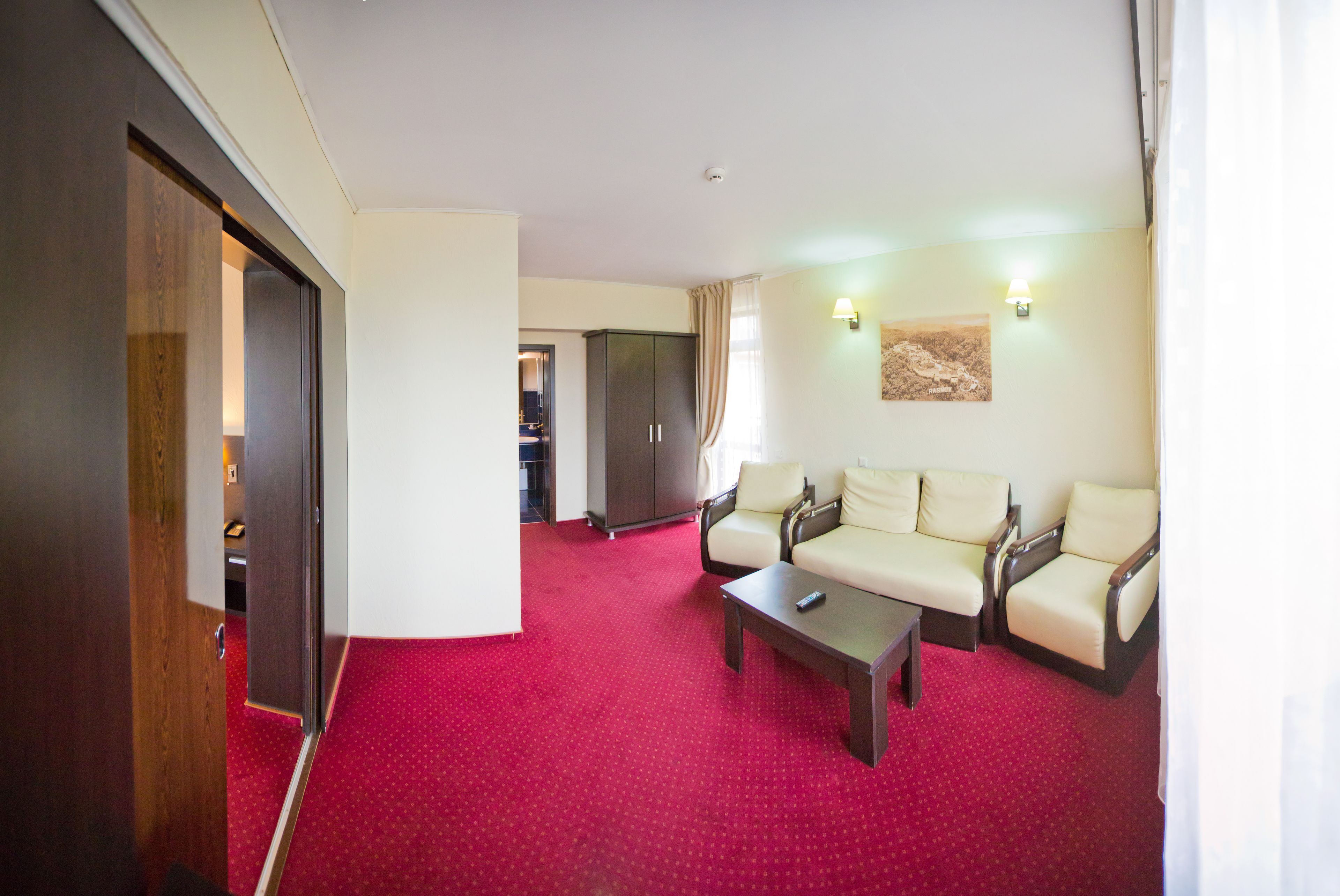 A hotel room with a red carpet, two sofas, a coffee table, and a wardrobe.