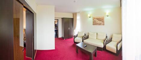 A hotel room with a red carpet, two sofas, a coffee table, and a wardrobe.