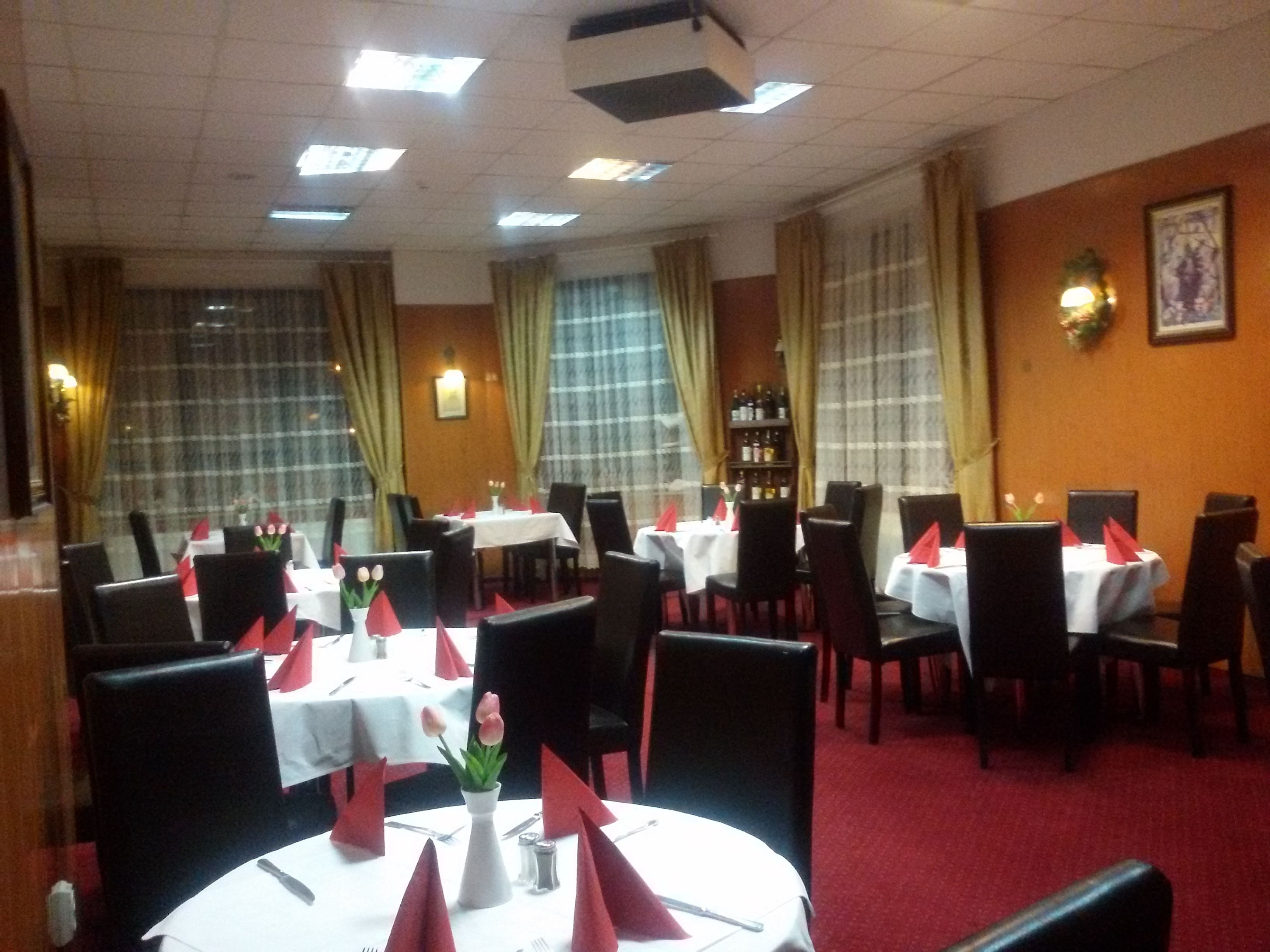 Un restaurante con mesas redondas, sillas negras y servilletas rojas.