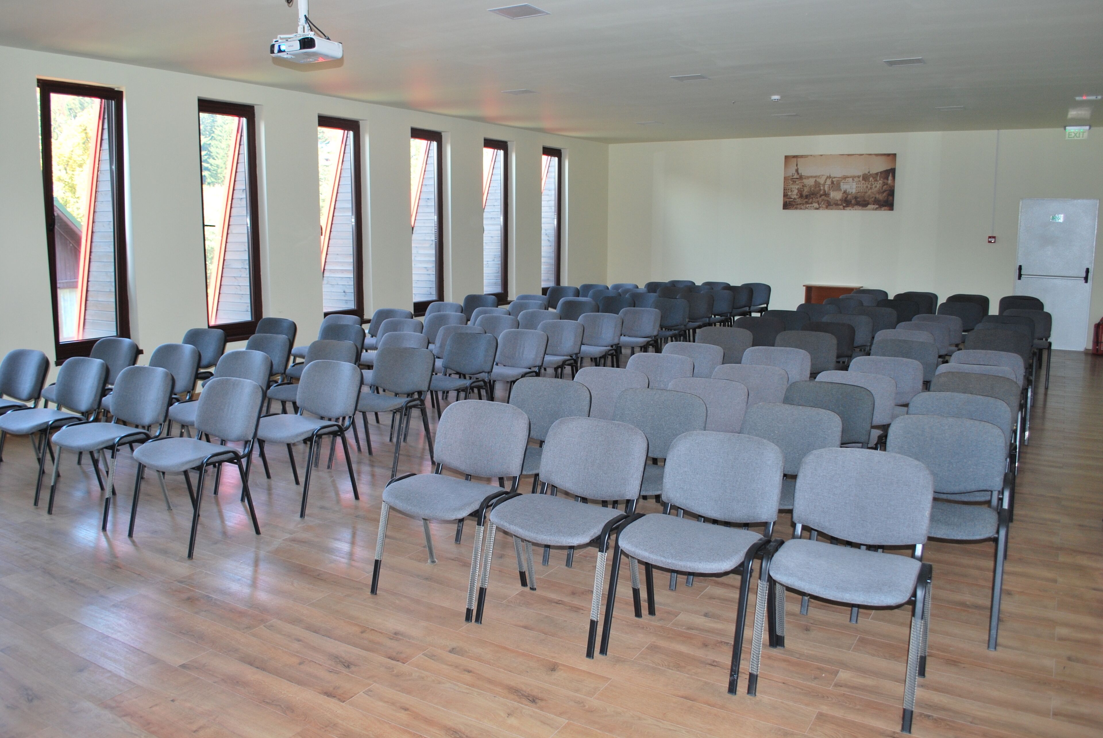 A conference room with rows of grey chairs, large windows, and a projector on the ceiling.