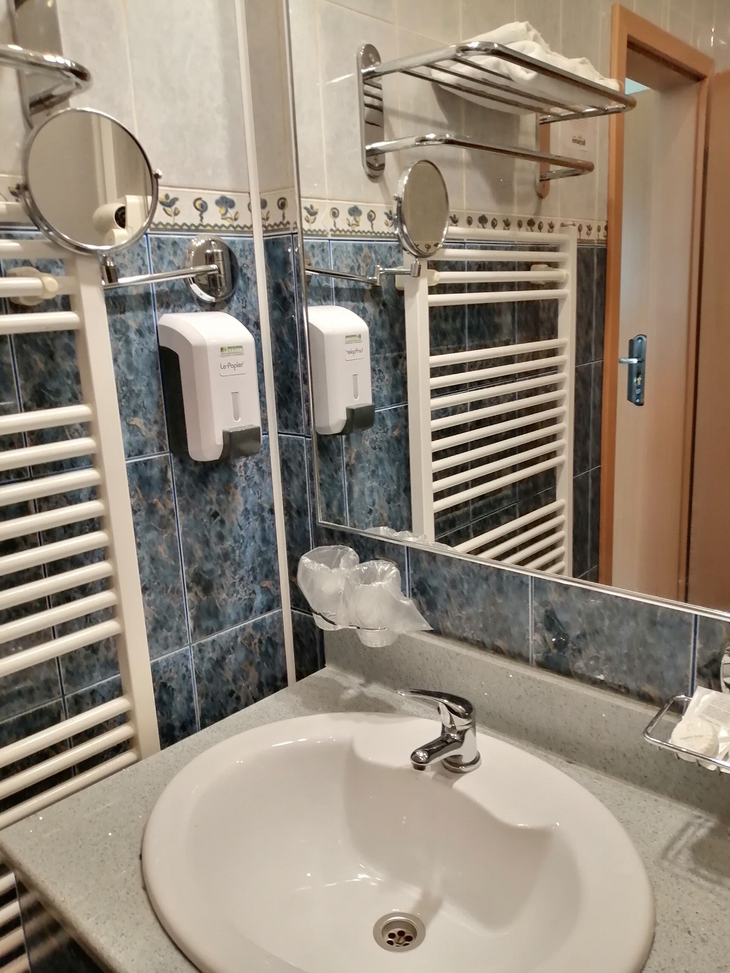 A bathroom with a sink, mirror, towel rack, and hand soap dispenser.
