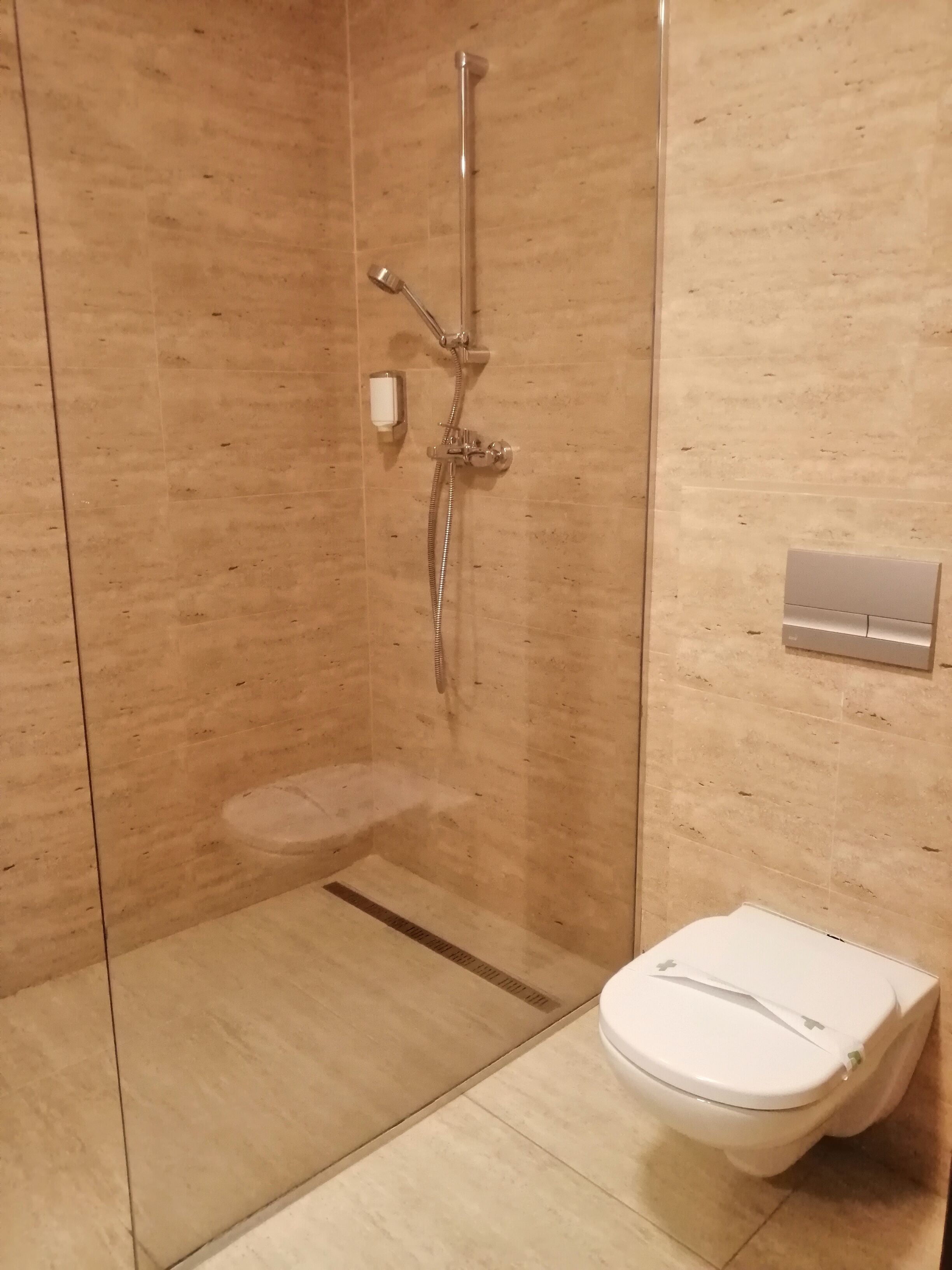 Uma casa de banho moderna com cabine de duche em vidro, sanita branca e painel de controlo fixado à parede.