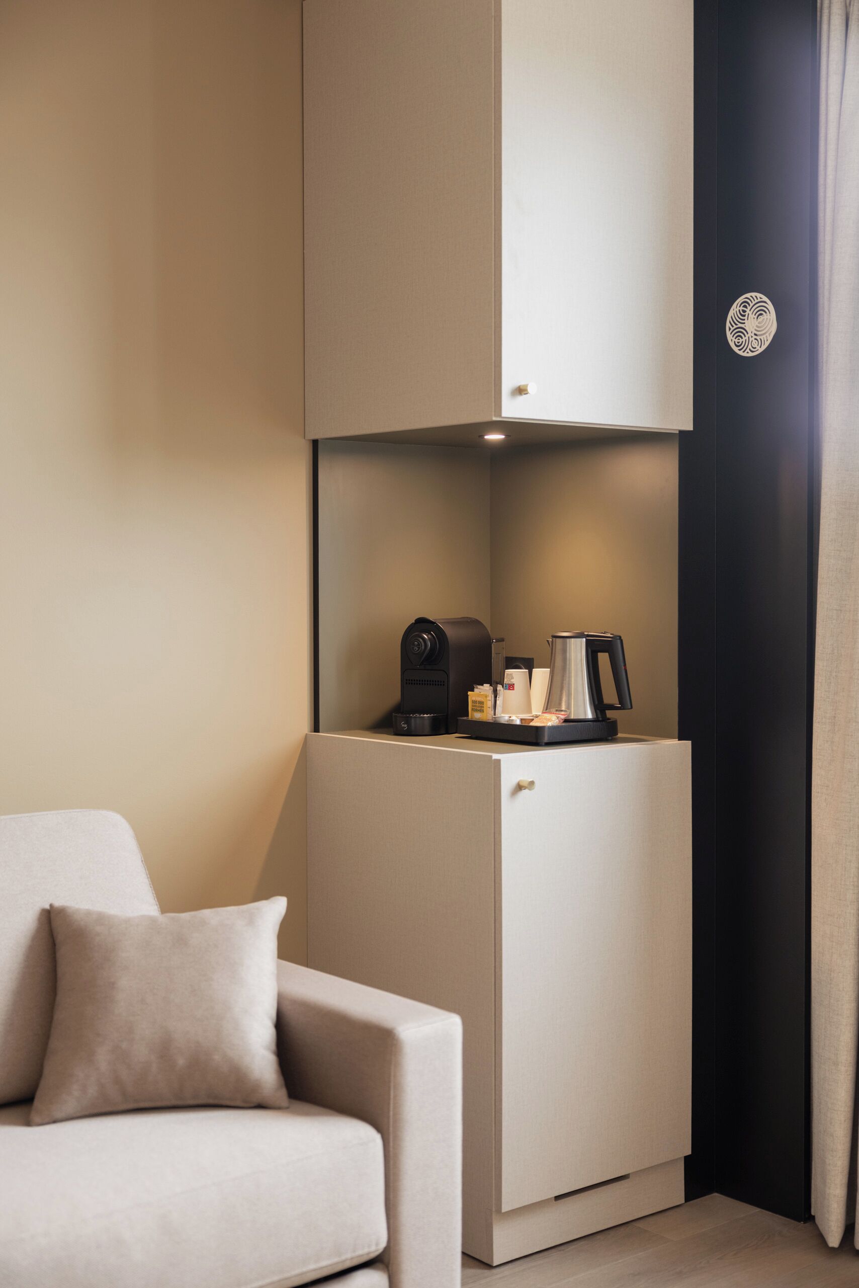 A compact hotel room with a sofa, a minibar, and a coffee machine.