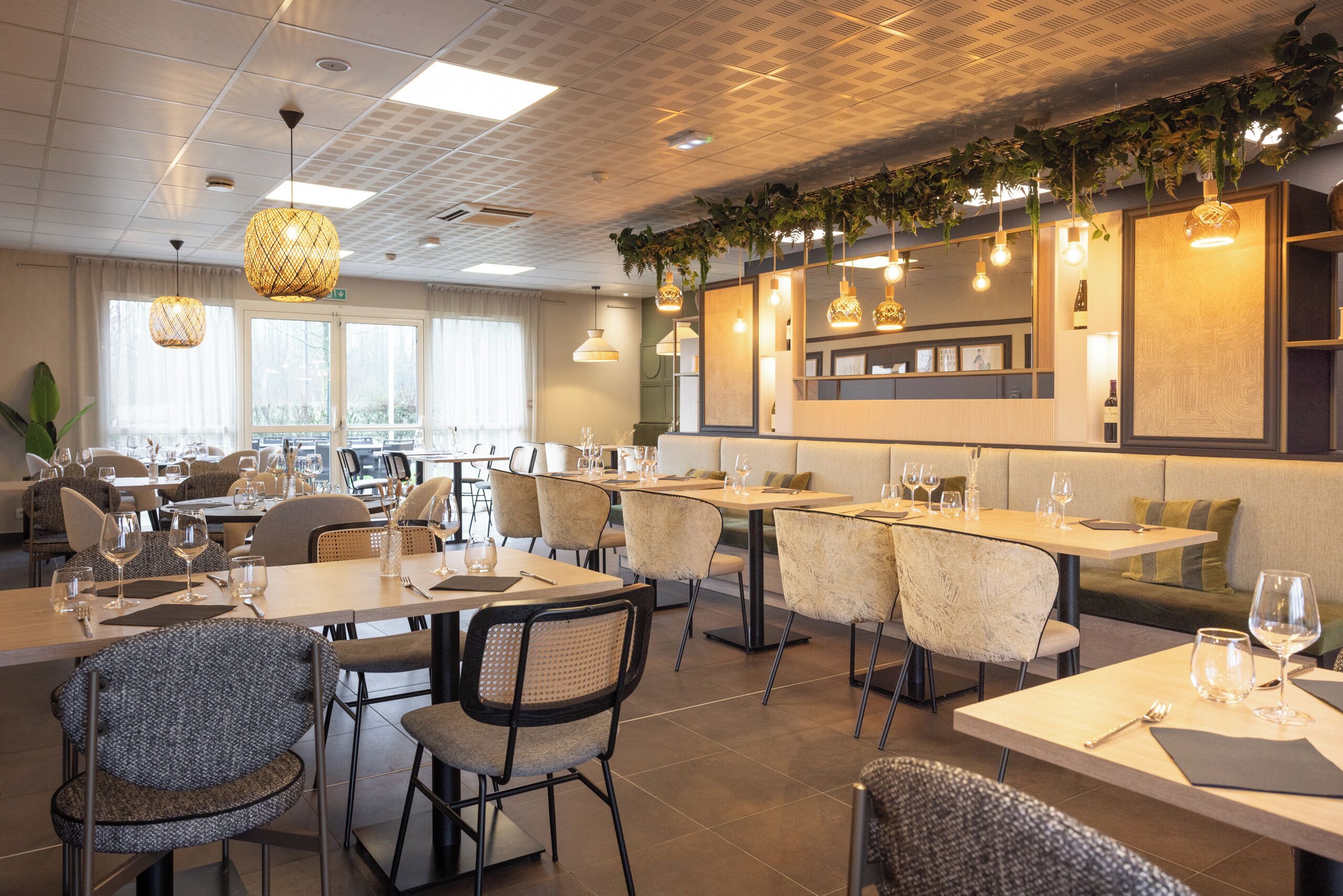 A modern restaurant with multiple dining areas, including booths and tables. There are hanging lights and a large mirror on the wall.