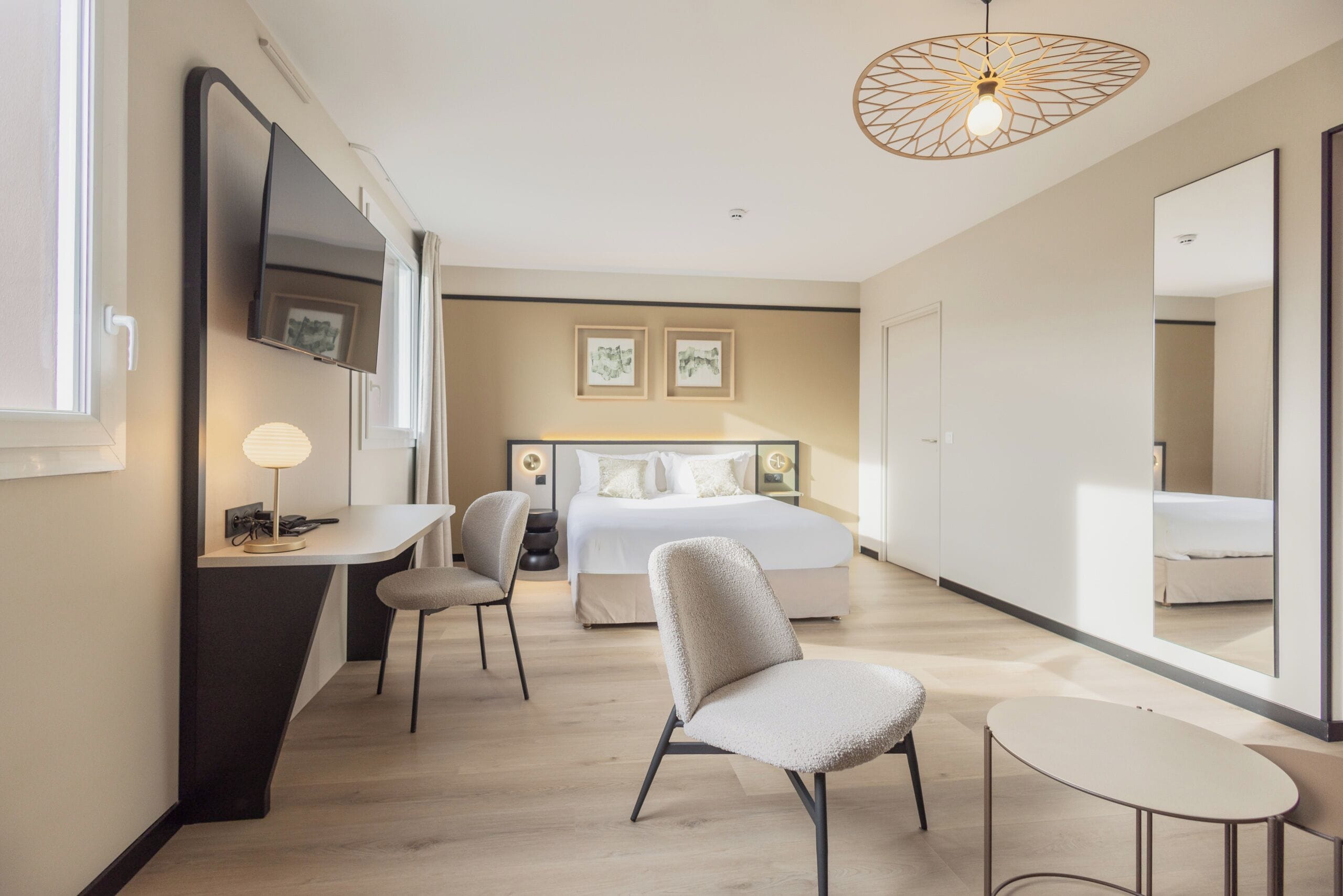 Una habitación de hotel moderna con una cama, un escritorio, una silla, una mesita y un espejo grande.