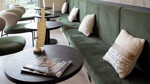 Un intérieur moderne avec un canapé vert, des tables rondes, des suspensions en osier et un grand miroir au mur.