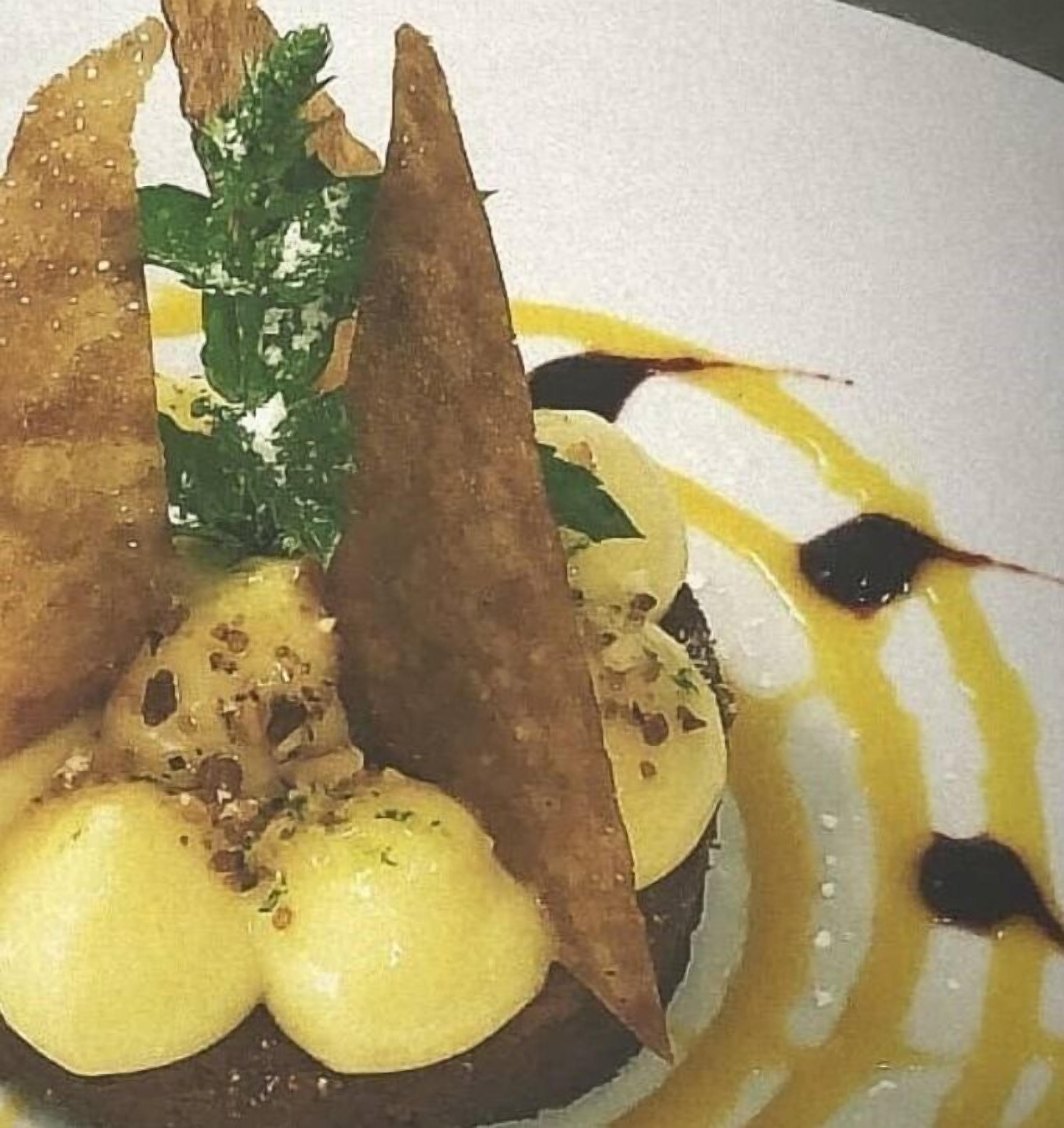 A dessert with a dark base, topped with a golden sauce and a green garnish.