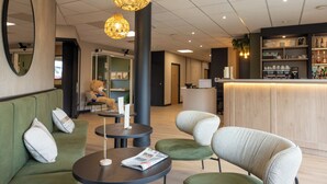 Un hall d’hôtel moderne avec des canapés verts, des tables rondes et un comptoir d’accueil.