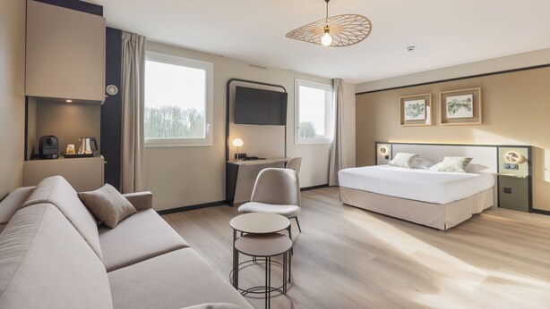 Une chambre d’hôtel moderne équipée d’un canapé, d’une petite table ronde, d’un lit, d’un bureau et d’une télévision.