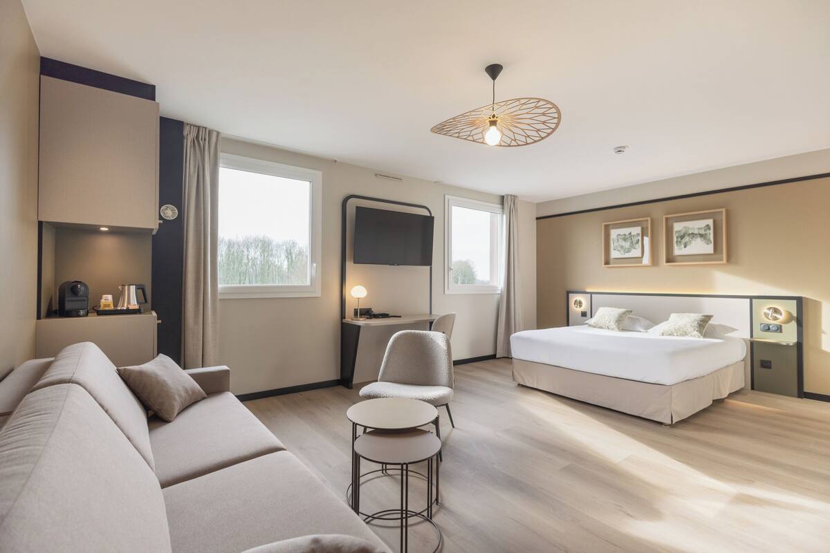 Une chambre d’hôtel moderne équipée d’un canapé, d’une petite table ronde, d’un lit, d’un bureau et d’une télévision.