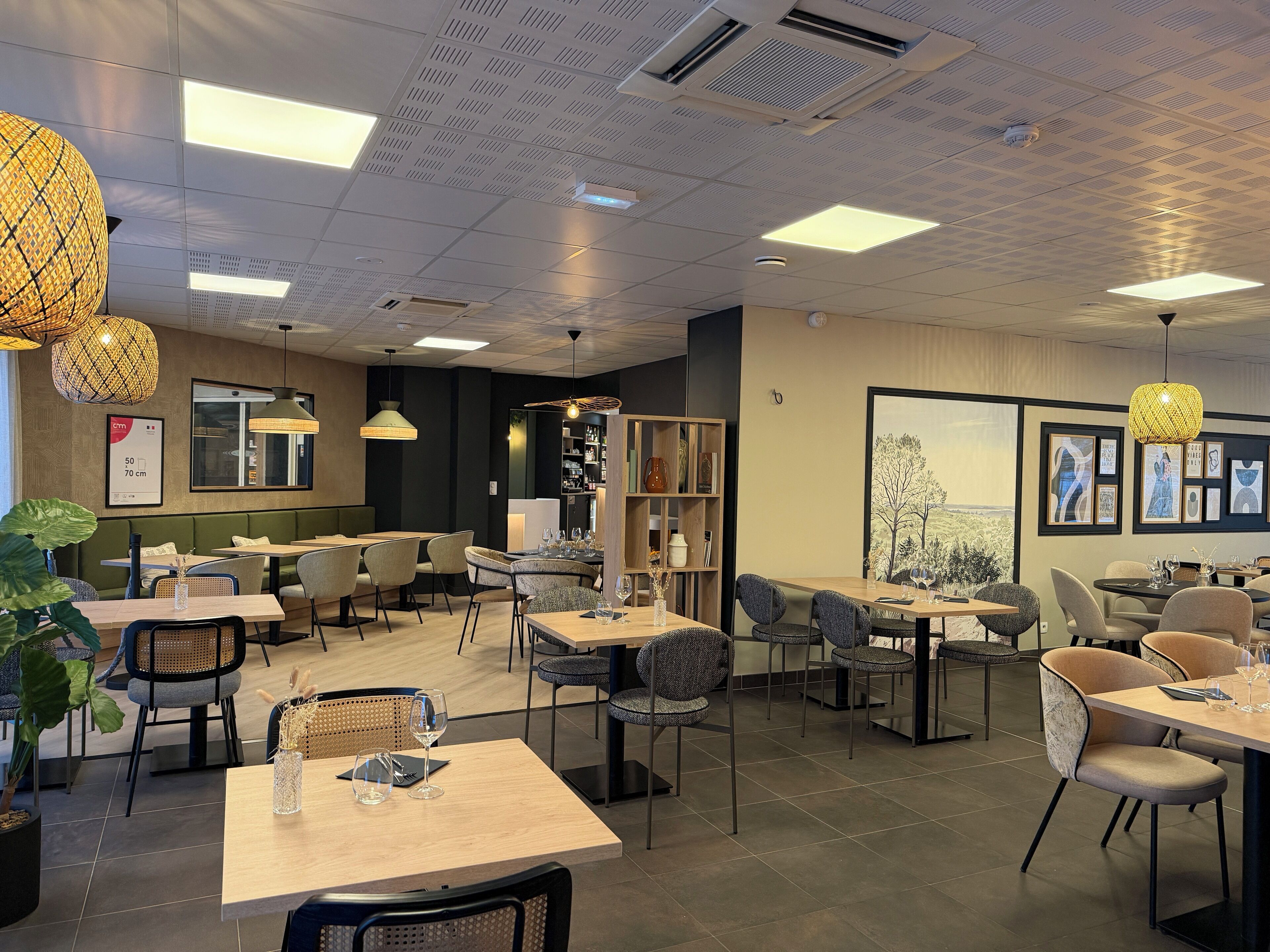 Un interior de restaurante moderno con varias mesas y sillas, iluminación colgante y vistas al exterior.