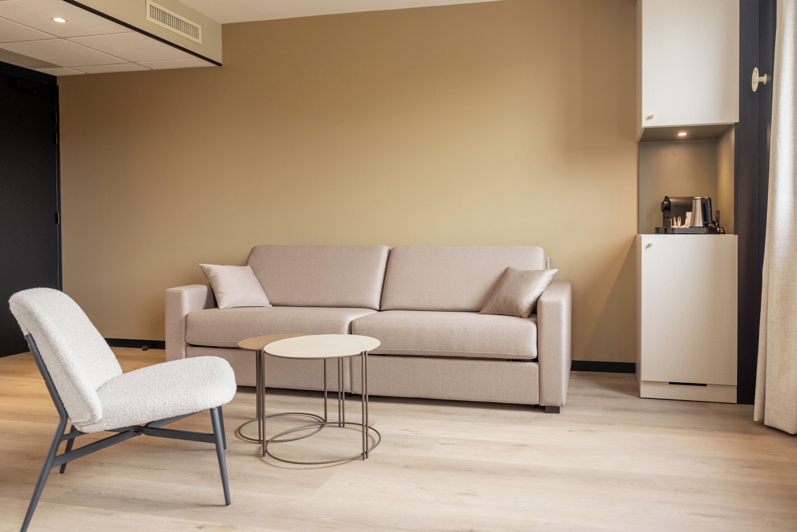 A modern living room with a beige sofa, a white armchair, and a small round table.