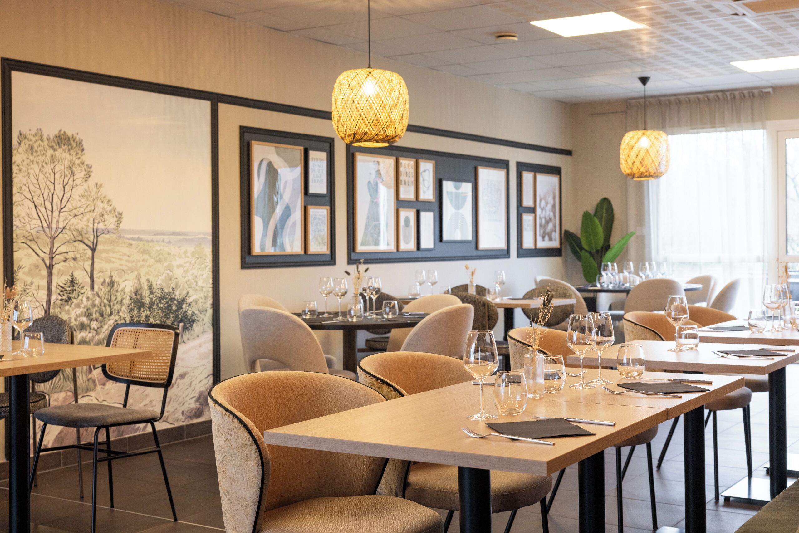 A restaurant with wooden tables and chairs, framed artwork on the walls, and hanging pendant lights.
