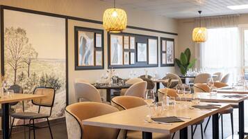 A restaurant with wooden tables and chairs, framed artwork on the walls, and hanging pendant lights.