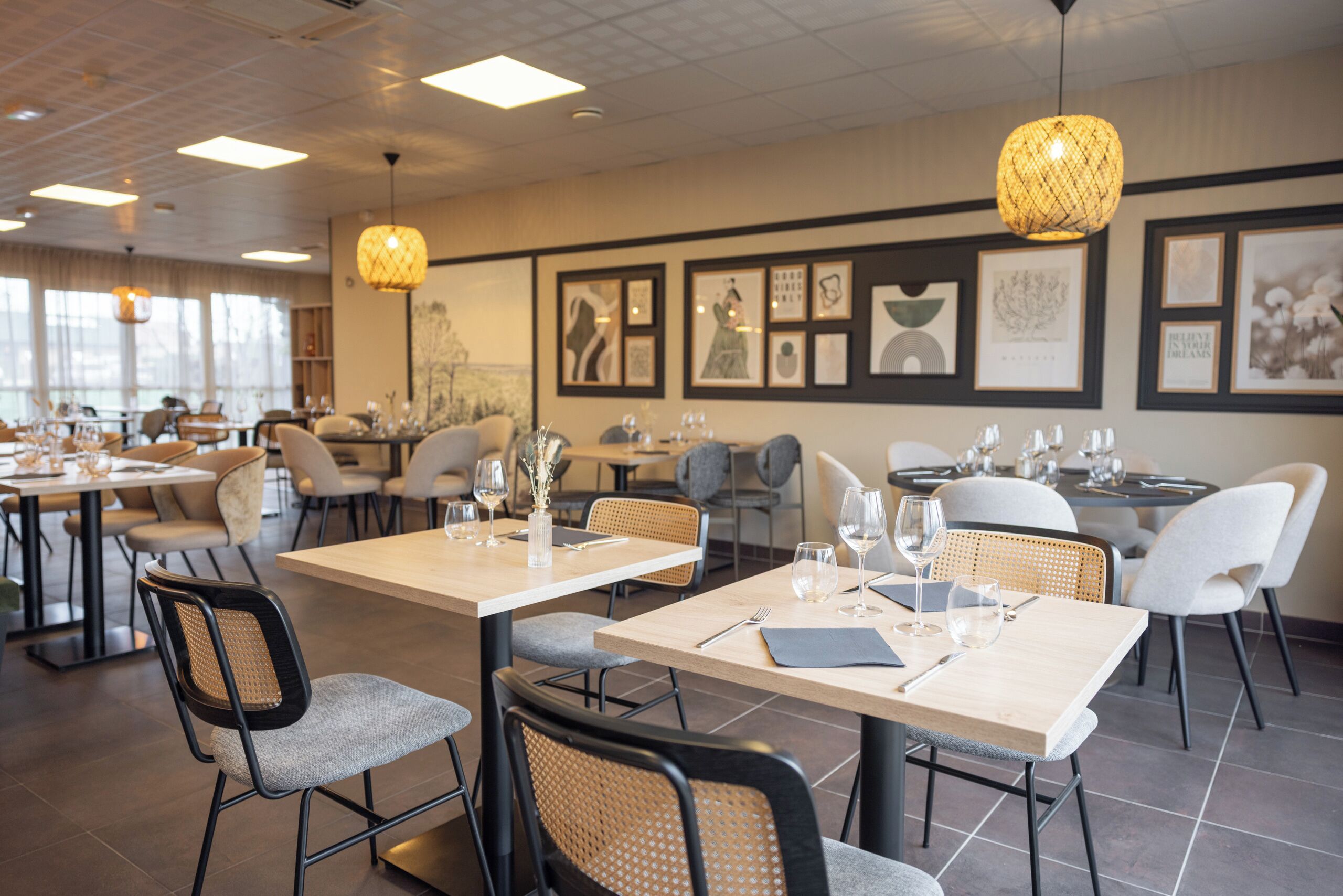 Un restaurant doté de nombreuses tables et chaises, avec des œuvres d’art encadrées accrochées aux murs et des luminaires suspendus.