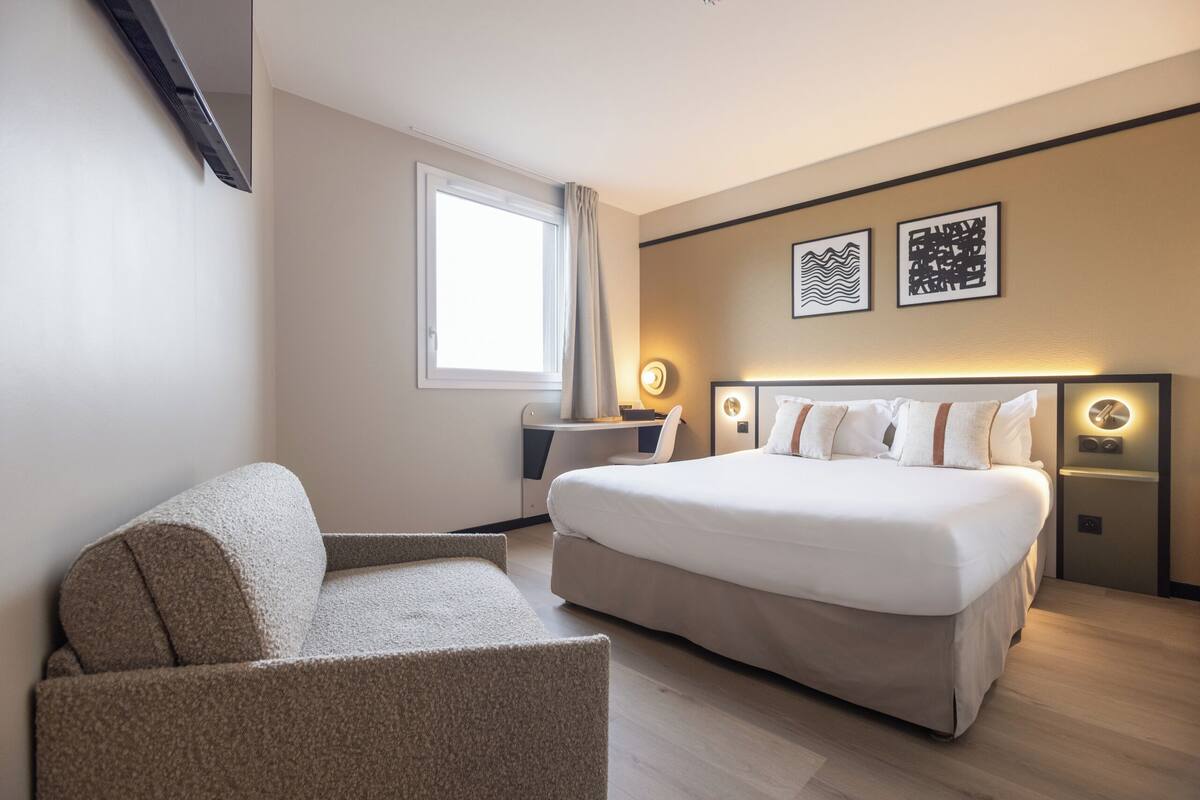 Une chambre d’hôtel moderne, dotée d’un grand lit, d’un canapé, d’un bureau et de deux lampes fixées au mur.