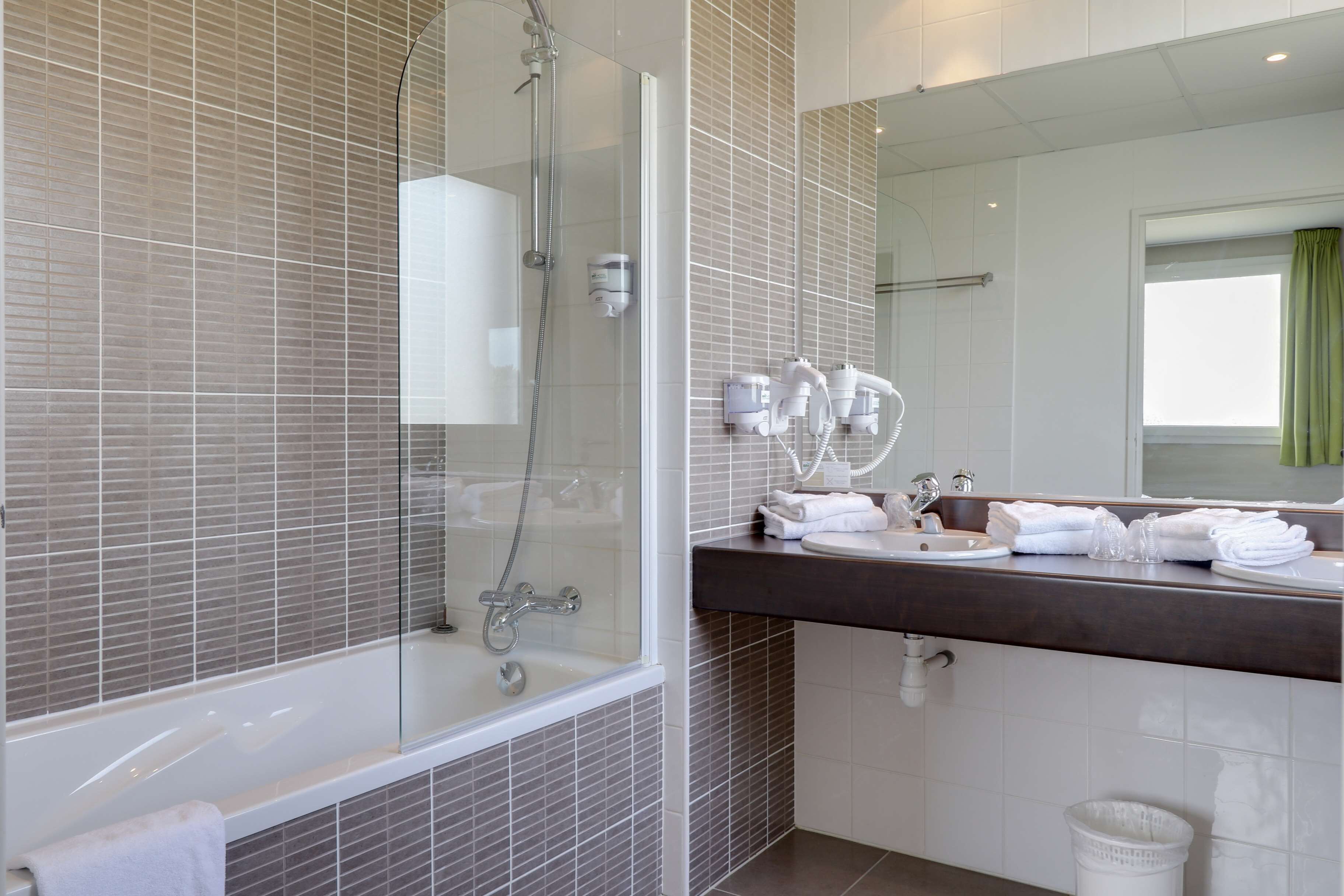 Ein modernes Badezimmer mit einer Glaskabine zur Dusche, einer dunklen Ablagefläche und einem großen Spiegel.