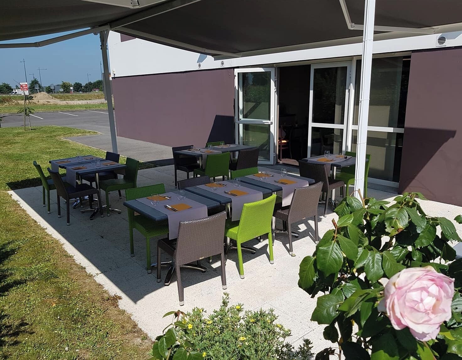 Un patio al aire libre con mesas y sillas, una zona de estar cubierta y la entrada a un edificio.