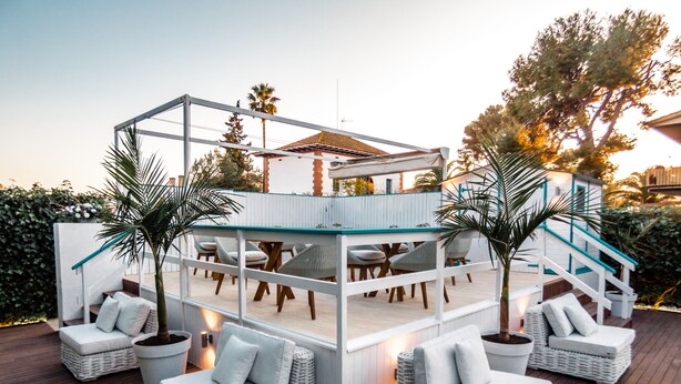 A covered outdoor seating area with wicker furniture and a glass railing. - Antonio S House (Sitges)