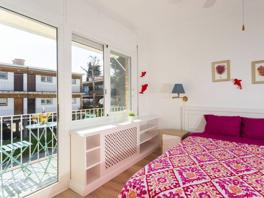 Ein Schlafzimmer mit großem Fenster, einem Balkon, einem Bett mit gemustertem Überwurf und einem kleinen Tisch mit Lampe.
