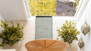 A modern room with a unique woven chair, a small wooden table, and a view of a garden through a skylight. - Antonio S House (Sitges)