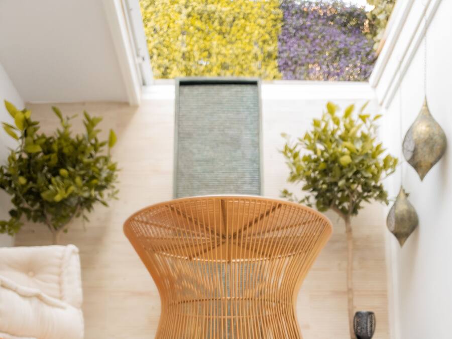 Una habitación moderna con una silla tejida original, una pequeña mesa de madera y vistas a un jardín a través de un tragaluz.
