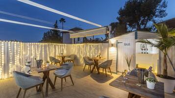 Un patio al aire libre con mobiliario de mimbre, una barra y luces colgantes.