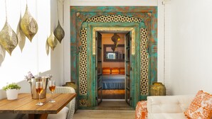 A room with a wooden table, two glasses of wine, a white sofa with orange pillows, and a decorative archway leading to a bedroom. - Antonio S House (Sitges)