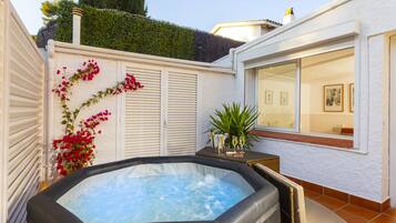 Un jacuzzi en un patio trasero con una cerca blanca, una ventana decorada con arte y una planta en maceta.