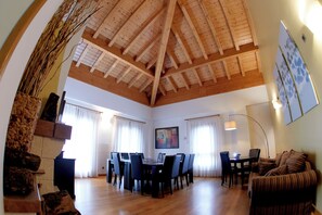 Un salón amplio con techo de madera alto, una zona de comedor con mesa y sillas, y un rincón de estar acogedor con sofá.