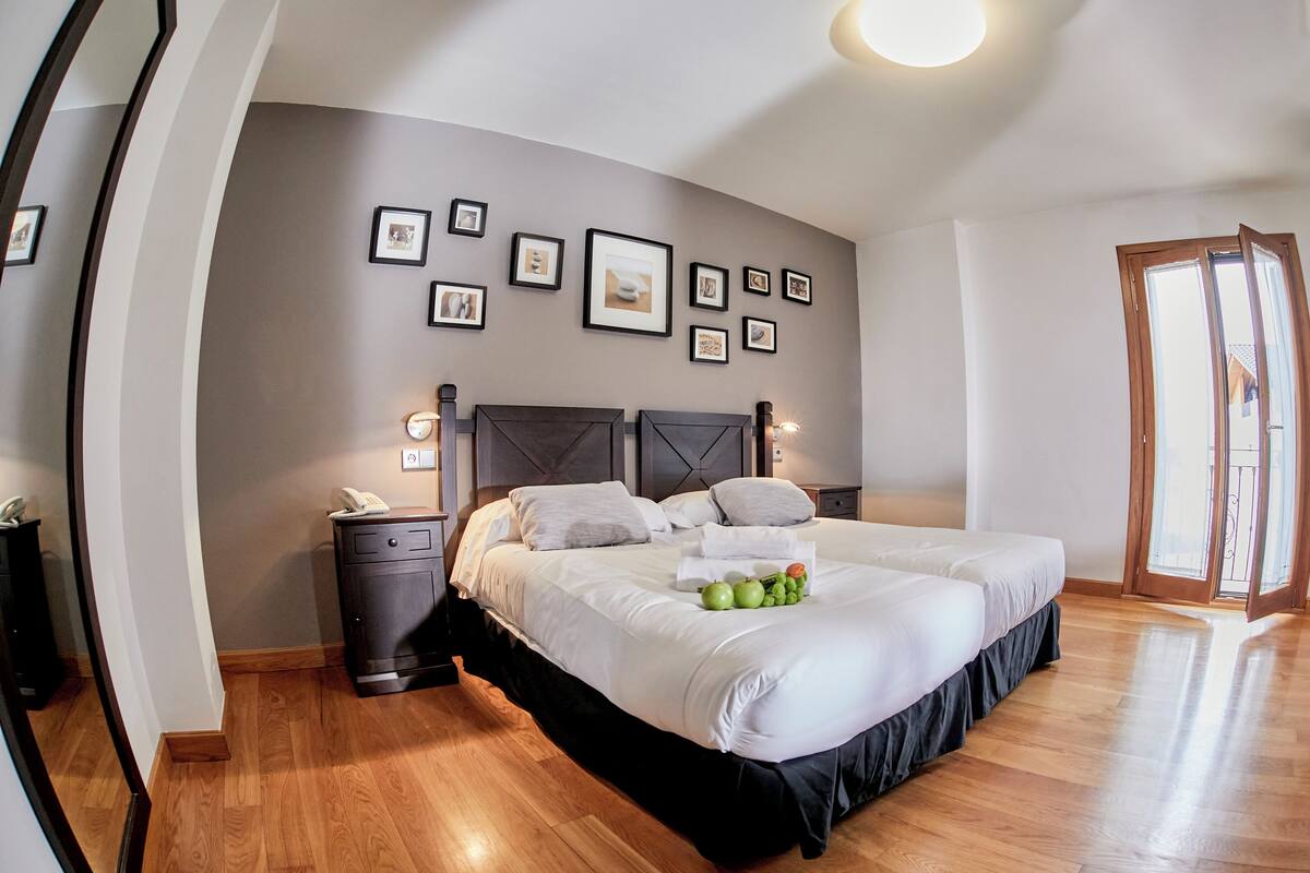 A bedroom with a large bed, a nightstand, a wall-mounted phone, and framed pictures.